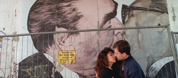 Two unidentified tourists kiss in front of a painting on one of the rare remaing parts of the Wall in Berlin, in October 1995 - Sputnik International