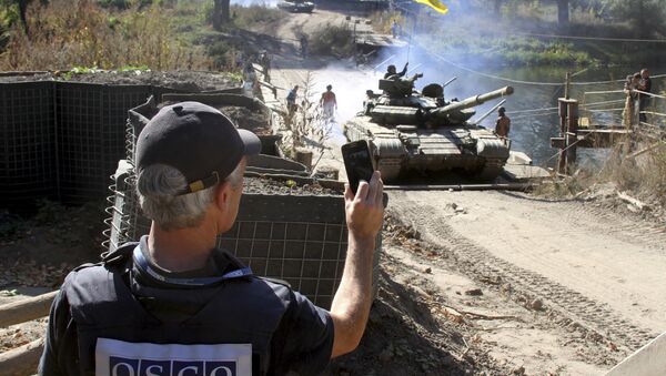 A member of the Organization for Security and Co-operation in Europe (OSCE) monitors the withdrawal of tanks of the Ukrainian armed forces near the village of Nyzhnje in Luhansk region, Ukraine, October 5, 2015 - Sputnik International