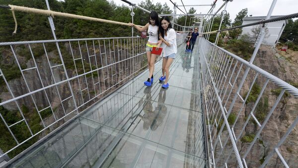 Tourists look down as they walk on a glass suspension bridge at the Shiniuzhai National Geo-park in Pinging county, Hunan province, China, September 24, 2015 - Sputnik International