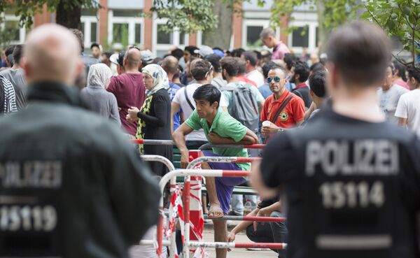 Police stand next to asylum seekers waiting in front of the reception center for refugees in Berlin, Germany, Friday, Aug. 7, 2015. Police stand next to asylum seekers waiting in front of the reception center for refugees in Berlin, Germany, Friday, Aug. 7, 2015. - Sputnik International