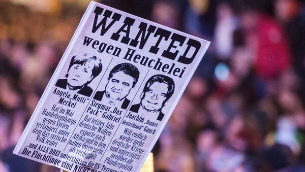 Protestors hold a banner with manipulated images of German Chancellor Angela Merkel, German Economy Minister Sigmar Gabriel and German President Joachim Gauck, from left to right, during a demonstration of the PEGIDA (Patriotic Europeans against the Islamization of the West), marking the first anniversary of the anti-Islam group in Dresden, eastern Germany, Monday, Oct. 19, 2015. - Sputnik International