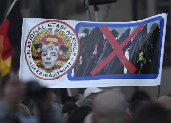 Protesters hold a poster depicting German Chancellor Angela Merkel with pig-ears beside women in burqas during a demonstration of PEGIDA (Patriotic Europeans against the Islamization of the West) in Dresden, eastern Germany, Monday, Oct. 5, 2015. Protesters hold a poster depicting German Chancellor Angela Merkel with pig-ears beside women in burqas during a demonstration of PEGIDA (Patriotic Europeans against the Islamization of the West) in Dresden, eastern Germany, Monday, Oct. 5, 2015. - Sputnik International