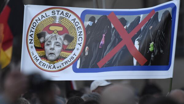 Protesters hold a poster depicting German Chancellor Angela Merkel with pig-ears beside women in burqas during a demonstration of PEGIDA (Patriotic Europeans against the Islamization of the West) in Dresden, eastern Germany, Monday, Oct. 5, 2015. - Sputnik International