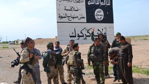 Iraqi Kurdish Peshmerga fighters stand next to an Islamic State (IS) group sign at the entrance to the northern Iraqi town of Hawija, south of Kirkuk on March 9, 2015 after they reportedly re-took the area from IS jihadists - Sputnik International