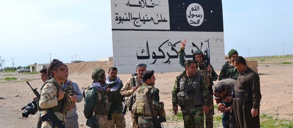 Iraqi Kurdish Peshmerga fighters stand next to an Islamic State (IS) group sign at the entrance to the northern Iraqi town of Hawija, south of Kirkuk on March 9, 2015 after they reportedly re-took the area from IS jihadists - Sputnik International