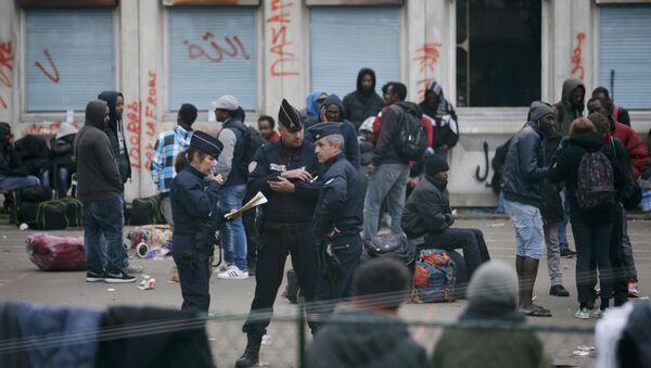 French police stand near migrants who gather in the courtyard of the Lycee Jean Quarre, an empty secondary school occuiped by hundred of migrants and asylum seekers in the 19th district in Paris, France, October 23, 2015 - Sputnik International