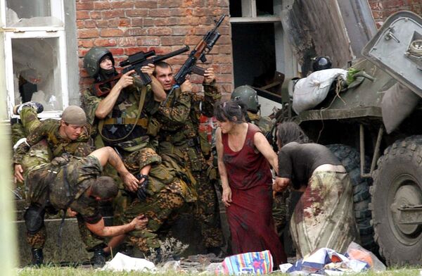 A Russian special police soldier (L) carries an injured colleague as two soldiers and two women take cover behind the APC during the rescue operation of Beslan's school, northern Ossetia, September 3,2004 - Sputnik International