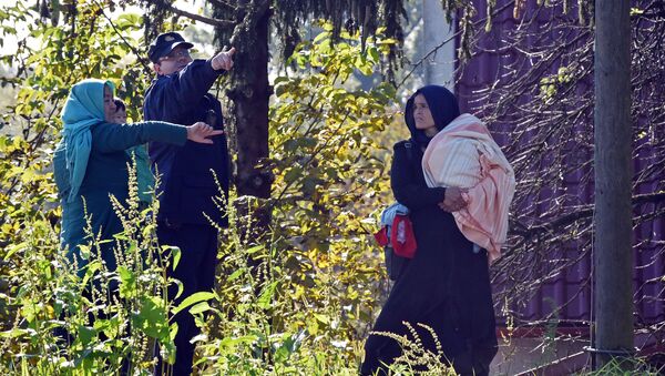 A Croatian police officer directs two women across the Sulta river as migrants and refugees travel across the Croatian-Slovenian border on October 20, 2015 near Kljuc Brdovecki - Sputnik International