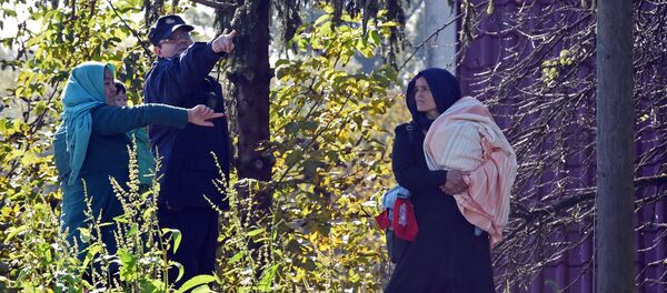 A Croatian police officer directs two women across the Sulta river as migrants and refugees travel across the Croatian-Slovenian border on October 20, 2015 near Kljuc Brdovecki A Croatian police officer directs two women across the Sulta river as migrants and refugees travel across the Croatian-Slovenian border on October 20, 2015 near Kljuc Brdovecki - Sputnik International