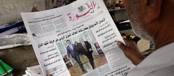 A picture taken on October 22, 2015 shows a Syrian man in Damascus holding an edition of Syrian al-Thawra (The Revolution) newspaper displaying a picture of President Bashar al-Assad with his Russian counterpart Vladimir Putin during the former's visit to Moscow. - Sputnik International