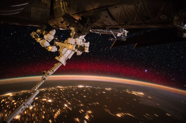 International Space Station crew members captured this view of the station's remote controlled Canadarm protruding from the orbiting laboratory, with Earth's colorful aurora, sparkling city lights and a rising sun over a background of stars. - Sputnik International