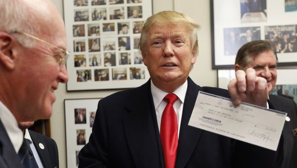 Secretary of State Bill Gardner watches at left as Republican presidential candidate Donald Trump shows off his filling fee check after filing papers to be on the nation's earliest presidential primary ballot. - Sputnik International