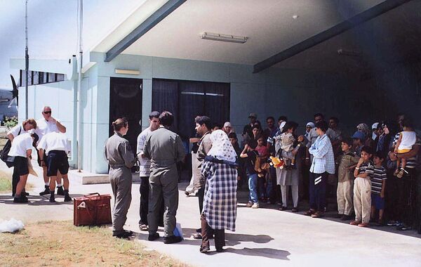 This file photo taken on August 19, 2001 shows officials (C-in green flight uniforms) questioning a refugee as other refugees (R), mostly believed to be from Iraq, wait in the shade before boarding an Australian Air Force Hercules aircraft on the Australian island territory of Christmas Island in the Indian Ocean. This file photo taken on August 19, 2001 shows officials (C-in green flight uniforms) questioning a refugee as other refugees (R), mostly believed to be from Iraq, wait in the shade before boarding an Australian Air Force Hercules aircraft on the Australian island territory of Christmas Island in the Indian Ocean. - Sputnik International
