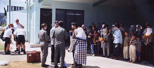 This file photo taken on August 19, 2001 shows officials (C-in green flight uniforms) questioning a refugee as other refugees (R), mostly believed to be from Iraq, wait in the shade before boarding an Australian Air Force Hercules aircraft on the Australian island territory of Christmas Island in the Indian Ocean. - Sputnik International