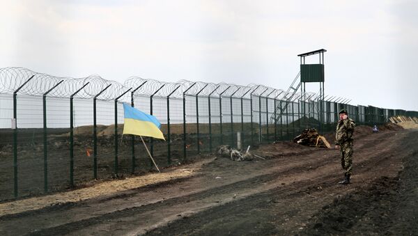 Ukrainian border guard officer speaks on a phone near a national flag attached to the fence on the Ukrainian-Russian border near Hoptivka, Kharkiv region, eastern Ukraine - Sputnik International
