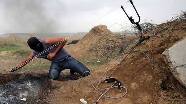 Палестинский демонстрант кидает камни из рогатки в израильских военых - Sputnik International