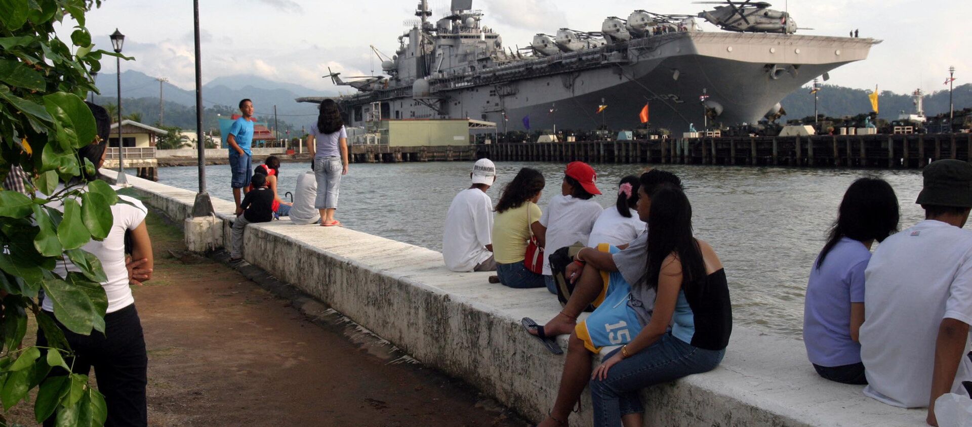People stand near the docked amphibious assault ship USS Essex at Subic Bay, Philippines. - Sputnik International, 1920, 28.01.2019