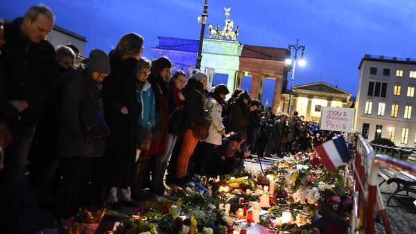 A banner reading 'We are Paris ' is pictured among candles and flowers in front of the Brandenbourg Gate outside the French embassy in Berlin, on November 14, 2015 a day after deadly attacks in Paris - Sputnik International