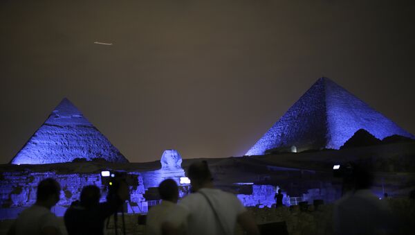 Egyptians watch the historical site of the Giza Pyramids as they are illuminated with blue light, as part of the celebration of the 70th anniversary of the United Nations, in Giza, just outside Cairo, Egypt, Saturday, Oct. 24, 2015 - Sputnik International