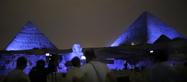Egyptians watch the historical site of the Giza Pyramids as they are illuminated with blue light, as part of the celebration of the 70th anniversary of the United Nations, in Giza, just outside Cairo, Egypt, Saturday, Oct. 24, 2015 - Sputnik International