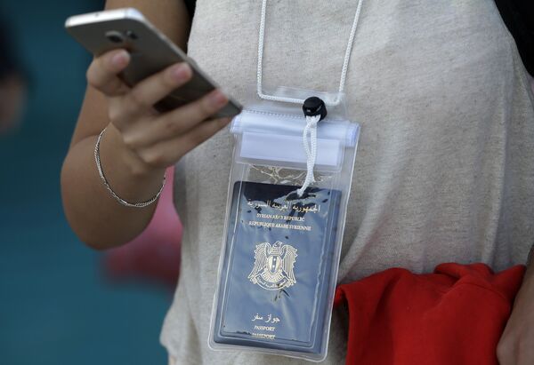 A Syrian woman uses her cell phone as she carries in a waterproof bag her passport after her arrival on a ferry from the Greek island of Lesbos at the Athens' port of Piraeus - Sputnik International