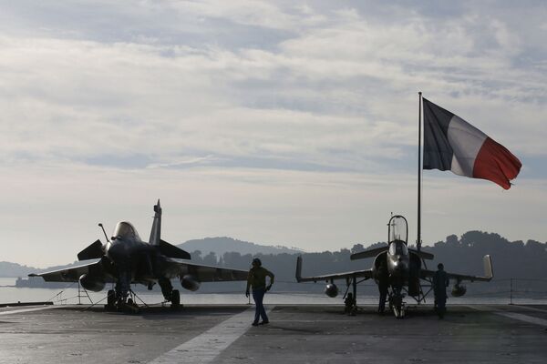 Flight deck crew work around a Rafale (L) and a Super Etendard fighter jets as a French flag flies aboard the French nuclear-powered aircraft carrier Charles de Gaulle before its departure from the naval base of Toulon, France, November 18, 2015 - Sputnik International