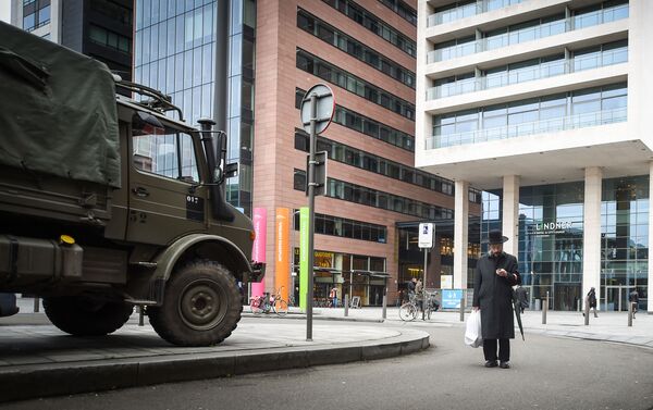 A man checks his mobile phone while walking by Belgian army trucks stationed in the Jewish neighborhood close to the Antwerp Central railway station in Antwerp, on November 20, 2015. - Sputnik International