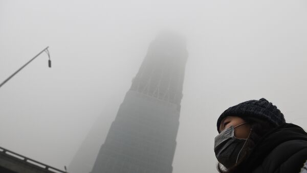 A woman waits for a bus below a skyscraper shrouded in smog on a heavily polluted day in Beijing on December 1, 2015 - Sputnik International