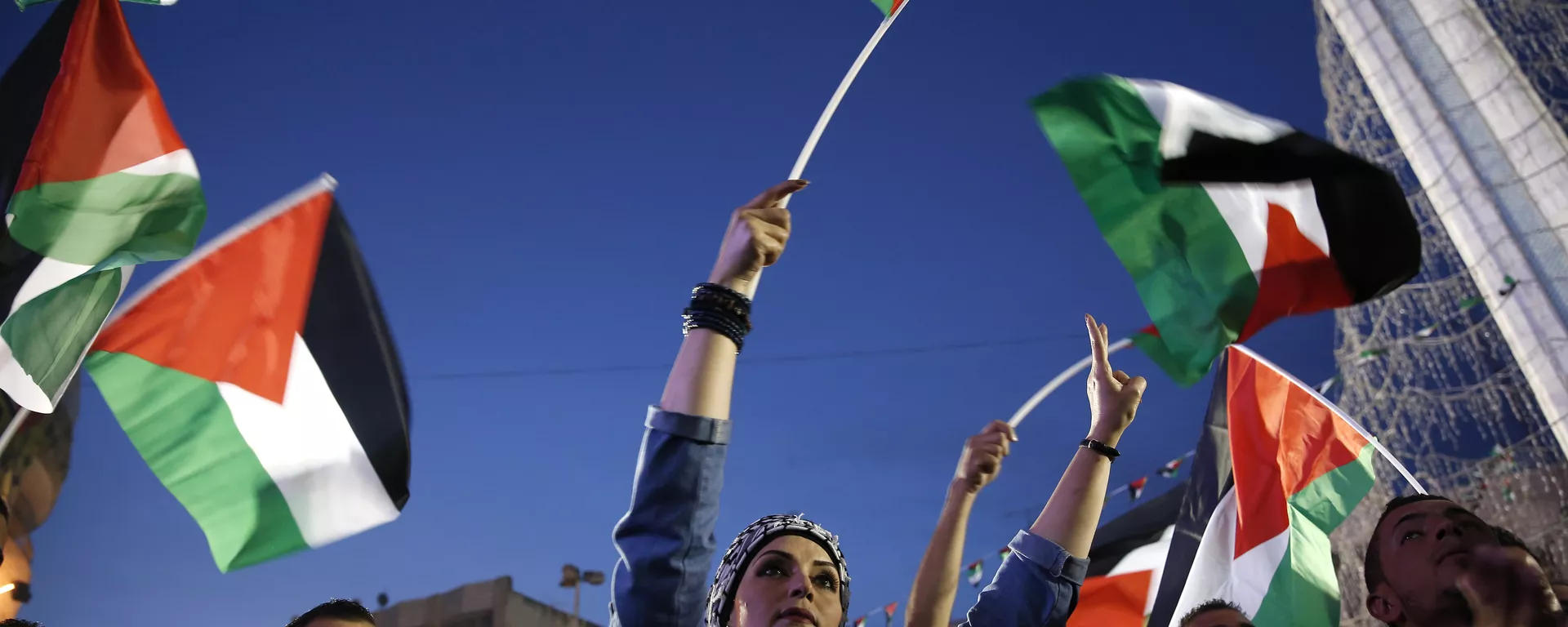 Palestinians wave their national flags as they watch a live-screening of president Mahmud Abbas' speech followed by the raising of the Palestinian flag at the United Nations headquarters in New York, on September 30, 2015 in the city of Ramallah - Sputnik International, 1920, 23.07.2024