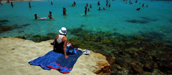 A woman sit on the sand as other people enjoy the sea at Nissi Beach in the famous southeastern coastal resort of Ayia Napa, Cyprus, Saturday, June 14, 2014 - Sputnik International