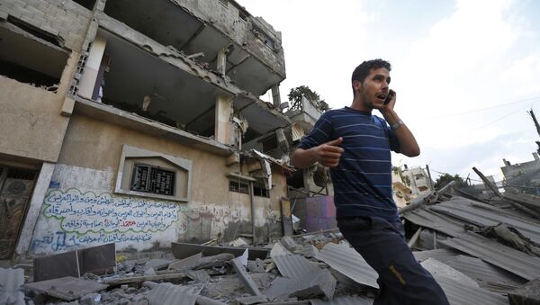 Palestinian talks on a mobile phone as he walks on the rubble of a damaged house following an overnight Israeli missile strike in Gaza City, Tuesday, July 15, 2014 - Sputnik International