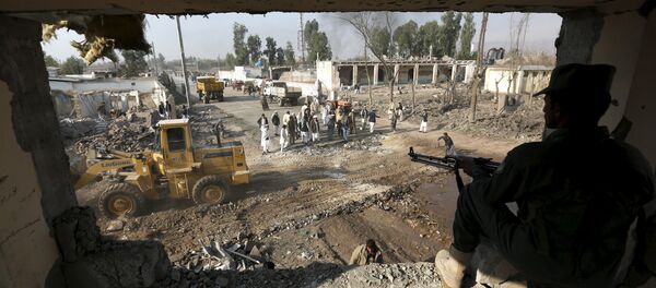 An Afghan policeman keeps watch while men gather at the site of a suicide car bomb attack in Surkhrod district of Nangarhar province, Afghanistan, December 7, 2015 - Sputnik International