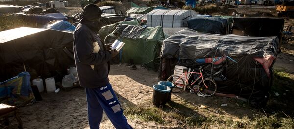 A man walks past a banner reading Pray for Deir Ezzor at the migrant camp known as the Jungle in Calais on December 7, 2015 A man walks past a banner reading Pray for Deir Ezzor at the migrant camp known as the Jungle in Calais on December 7, 2015 - Sputnik International