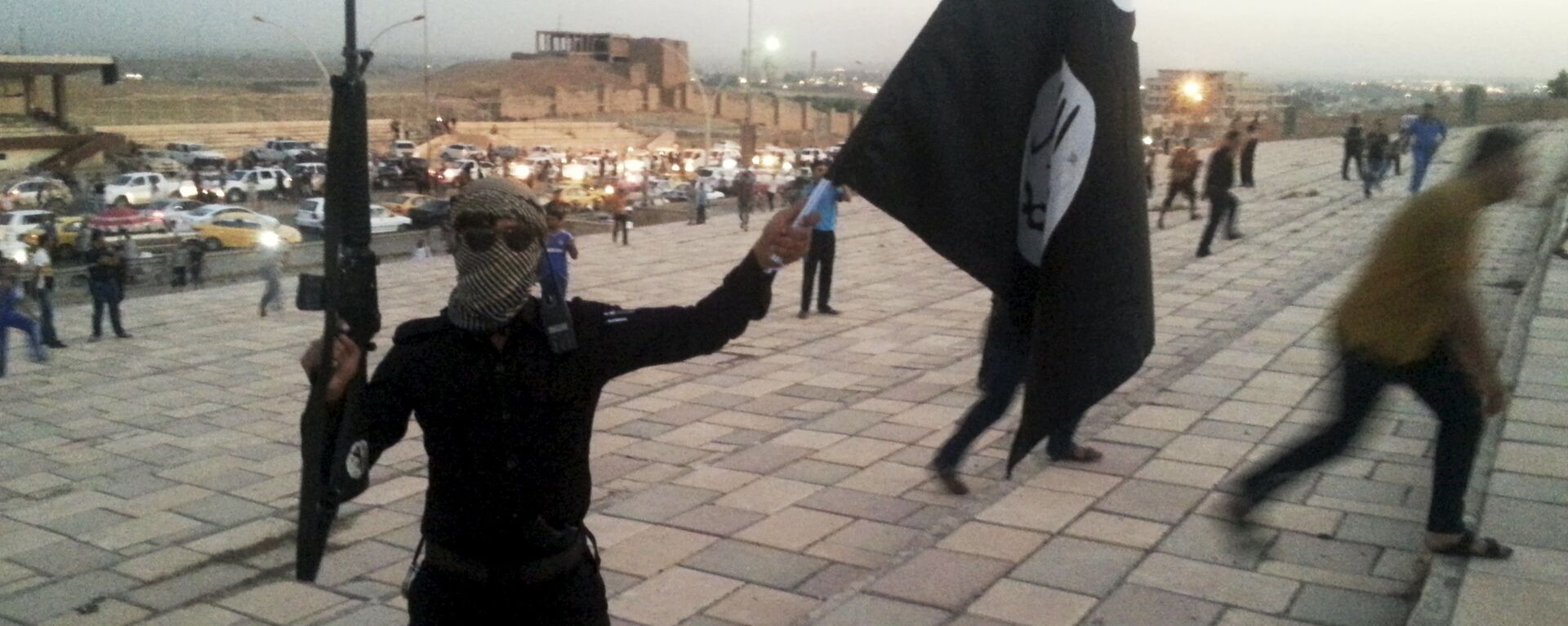 A fighter of Daesh holds an ISIL flag and a weapon on a street in the city of Mosul, Iraq, in this June 23, 2014. - Sputnik International, 1920, 04.08.2018