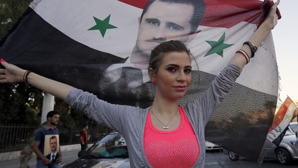 A Syrian girl holds her national flag bearing a portrait of Syria's President Bashar al-Assad - Sputnik International