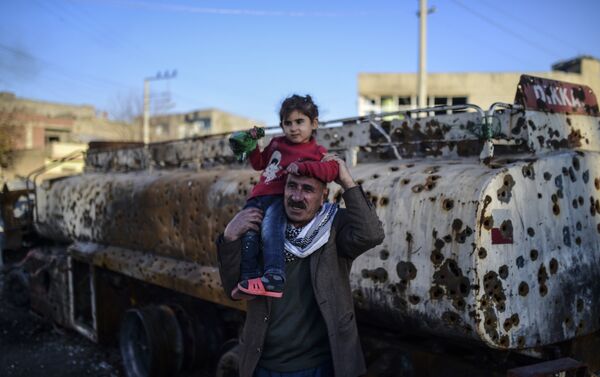 A man carries his daughter past a destroyed tanker truck in the southeastern city of Nusaybin, on December 24, 2015, in Mardin province. - Sputnik International