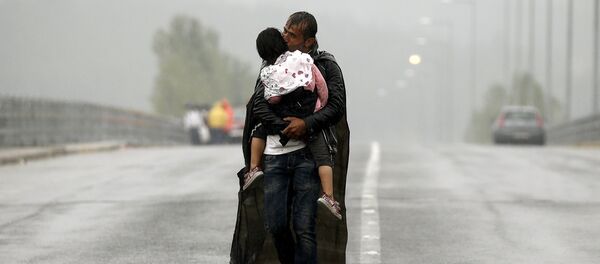 A Syrian refugee kisses his daughter as he walks through a rainstorm towards Greece's border with Macedonia, near the Greek village of Idomeni, September 10, 2015 - Sputnik International