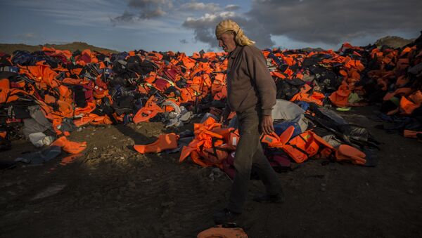 A man walks across piles of life jackets used by refugees and migrants to cross the Aegean sea from the Turkish coast. - Sputnik International