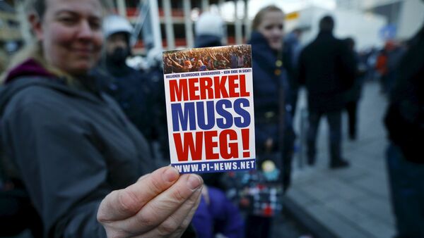 A supporter of the anti-immigration right-wing movement PEGIDA (Patriotic Europeans Against the Islamisation of the West) holds up a sticker for a photo during a demonstration rally in Cologne, Germany January 9, 2016. The sticker reads, Merkel must go! - Sputnik International