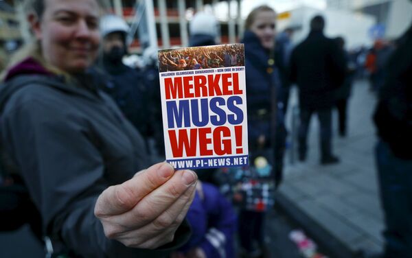 A supporter of the anti-immigration right-wing movement PEGIDA (Patriotic Europeans Against the Islamisation of the West) holds up a sticker for a photo during a demonstration rally in Cologne, Germany January 9, 2016. The sticker reads, Merkel must go! A supporter of the anti-immigration right-wing movement PEGIDA (Patriotic Europeans Against the Islamisation of the West) holds up a sticker for a photo during a demonstration rally in Cologne, Germany January 9, 2016. The sticker reads, Merkel must go! - Sputnik International
