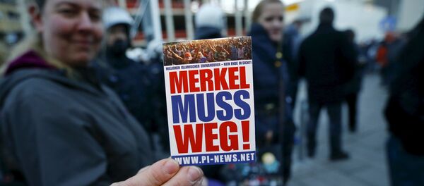 A supporter of the anti-immigration right-wing movement PEGIDA (Patriotic Europeans Against the Islamisation of the West) holds up a sticker for a photo during a demonstration rally in Cologne, Germany January 9, 2016. The sticker reads, Merkel must go! A supporter of the anti-immigration right-wing movement PEGIDA (Patriotic Europeans Against the Islamisation of the West) holds up a sticker for a photo during a demonstration rally in Cologne, Germany January 9, 2016. The sticker reads, Merkel must go! - Sputnik International