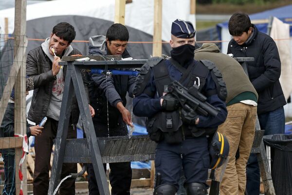 A French riot police officer (CRS) stands guard as migrants brush their teeth in a makeshift camp in what is known as the Jungle, a squalid sprawling camp in Calais, northern France, January 11, 2016. - Sputnik International