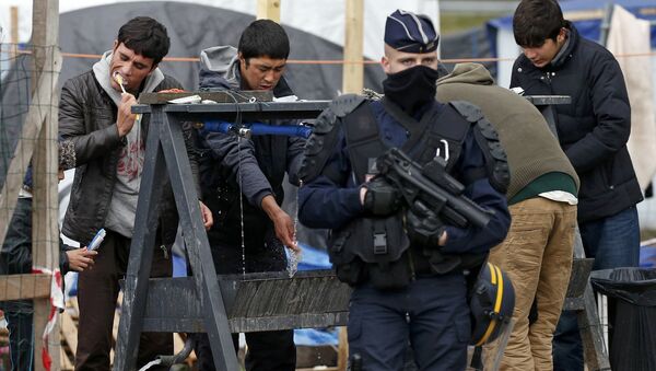 A French riot police officer (CRS) stands guard as migrants brush their teeth in a makeshift camp in what is known as the Jungle, a squalid sprawling camp in Calais, northern France, January 11, 2016. - Sputnik International