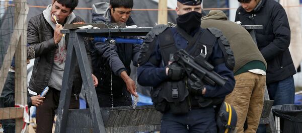 A French riot police officer (CRS) stands guard as migrants brush their teeth in a makeshift camp in what is known as the Jungle, a squalid sprawling camp in Calais, northern France, January 11, 2016. - Sputnik International