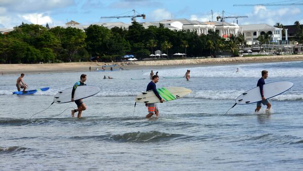 Foreign tourists hold surf boards as they wade into the waters off Kuta beach, Bali island - Sputnik International