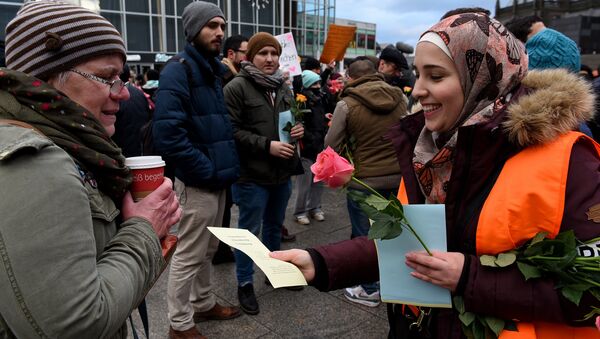 Refugees from Syria present flowers to passers-by as they demonstrate against violence near the Cologne main train station in Cologne, western Germany on January 16, 2016, where hundreds of women were groped and robbed in a throng of mostly Arab and North African men during New Year's festivities - Sputnik International