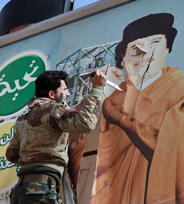 Libyan opposition supporter uses knife to cut a poster of Muammar Gaddafi in the captured rebel town of Ras Lanuf in the east of the country - Sputnik International