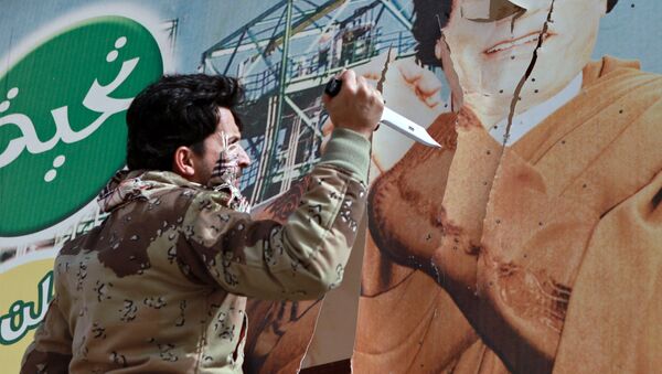 Libyan opposition supporter uses knife to cut a poster of Muammar Gaddafi in the captured rebel town of Ras Lanuf in the east of the country - Sputnik International