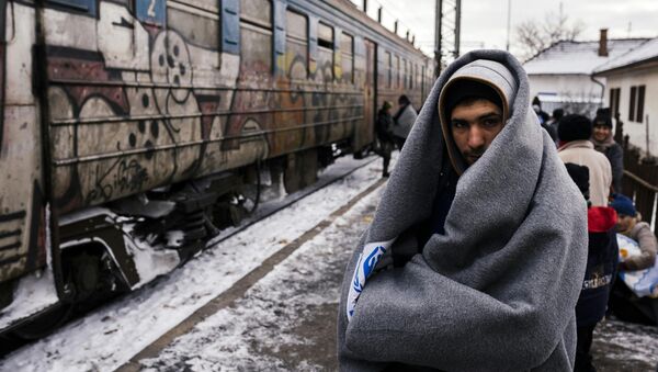 A migrant wrapped in a blanket to keep warm, waits with other migrants and refugees to board a train heading to the border with Croatia at the train station in Presevo, on January 19, 2016, after crossing the Macedonian border into Serbia - Sputnik International
