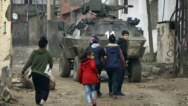 Backdropped by a Turkish forces armoured personnel carrier, residents walk around after the 24-hour curfew was lifted, in the mostly-Kurdish town of Silopi, in southeastern Turkey, near the border with Iraq, Tuesday, Jan. 19, 2016 - Sputnik International